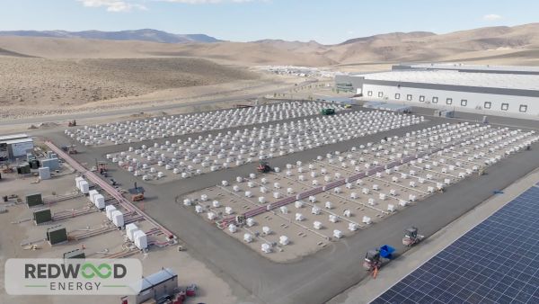 Aerial photo of parking lot-sized array of white battery modules adjacent to a photovoltaic array and large building