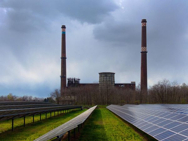 An old energy plant with cooling towers behind a field of new solar panels.