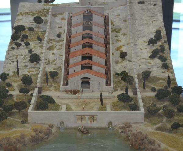 Photo of a museum model of the Roman waterwheel-powered flour mill at Barbegal, France, showing 8 connected buildings stepping down a steep hillside, with a pair of waterwheels at each step.