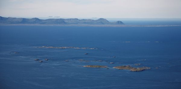 Aerial view of Andfjorden shows small islands in the foreground and mountain fjords in the distance. The water and air look cold.