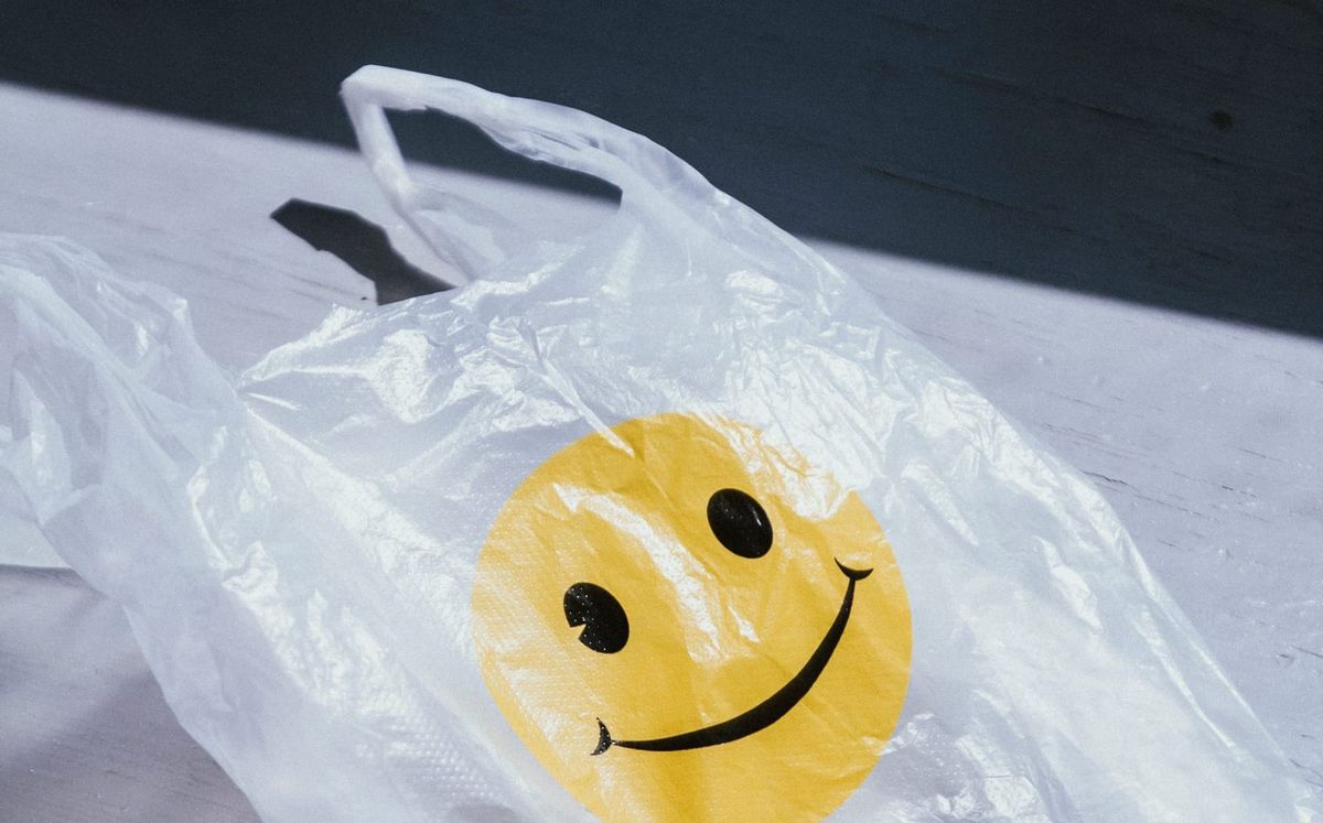 A photograph of a clear plastic bag with a yellow smily face image. The bag is in direct sunlight.