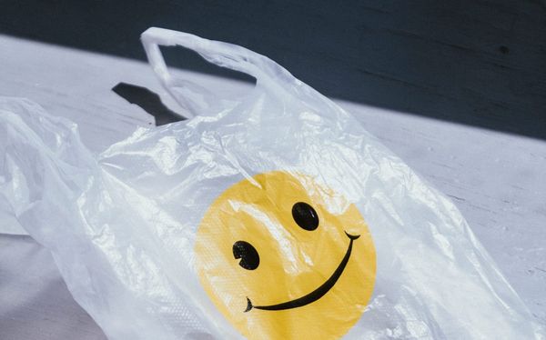 A photograph of a clear plastic bag with a yellow smily face image. The bag is in direct sunlight.