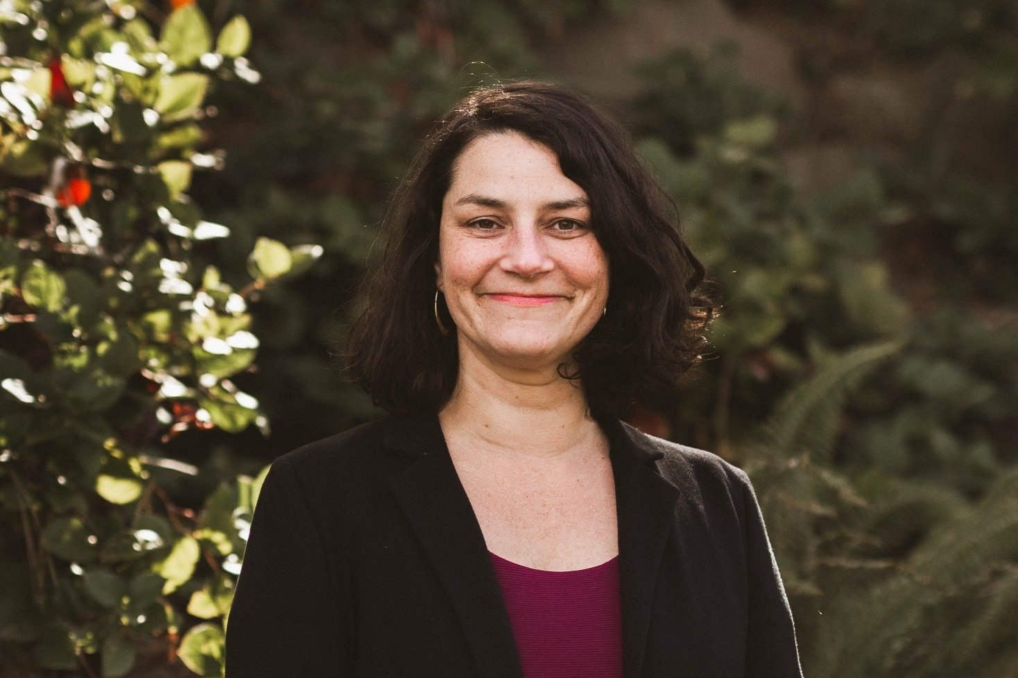 A portrait of Emily Alvarado, smiling towards the camera, infront of some plants.