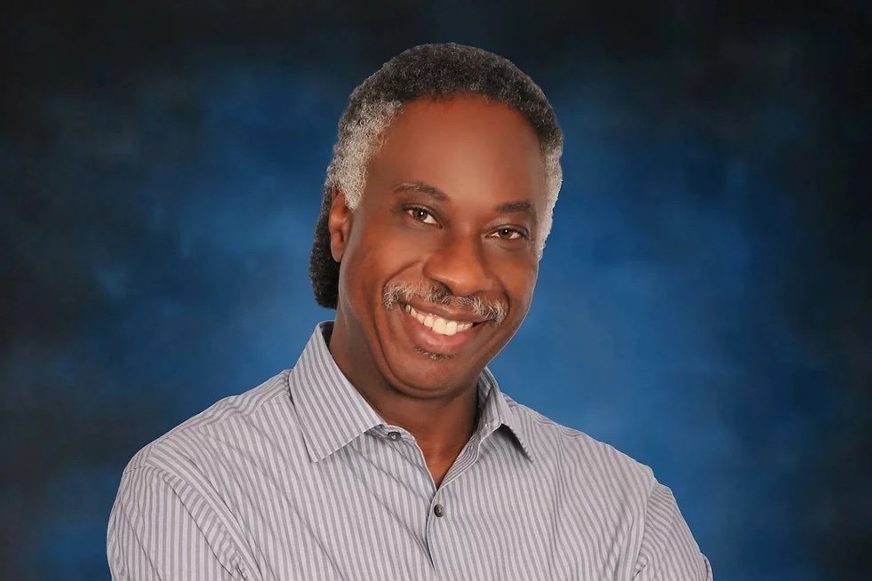 A portrait of Carey Anderson smiling towards the camera infront of a blue background.
