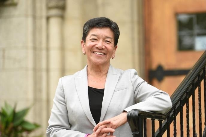 A portrait of Justice Mary Yu, smiling towards the camera, standing leaning against an exterior railing.