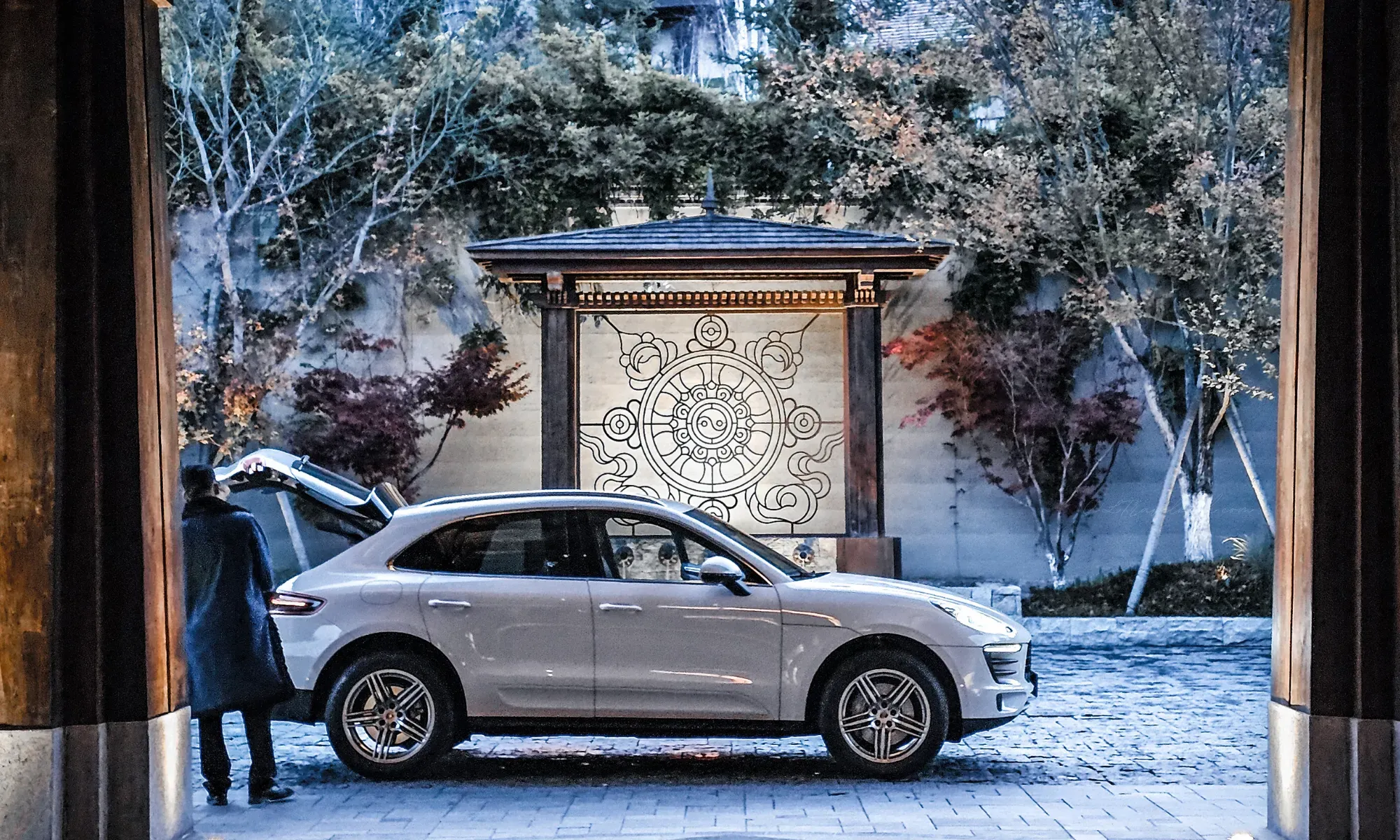 Close-up capture of the luxury arrival experience at Rissai Valley, showing a luxury white SUV parked on the stone driveway with a staff member attending to a guest, set against the resort's traditional architecture, by WLTravelbook
