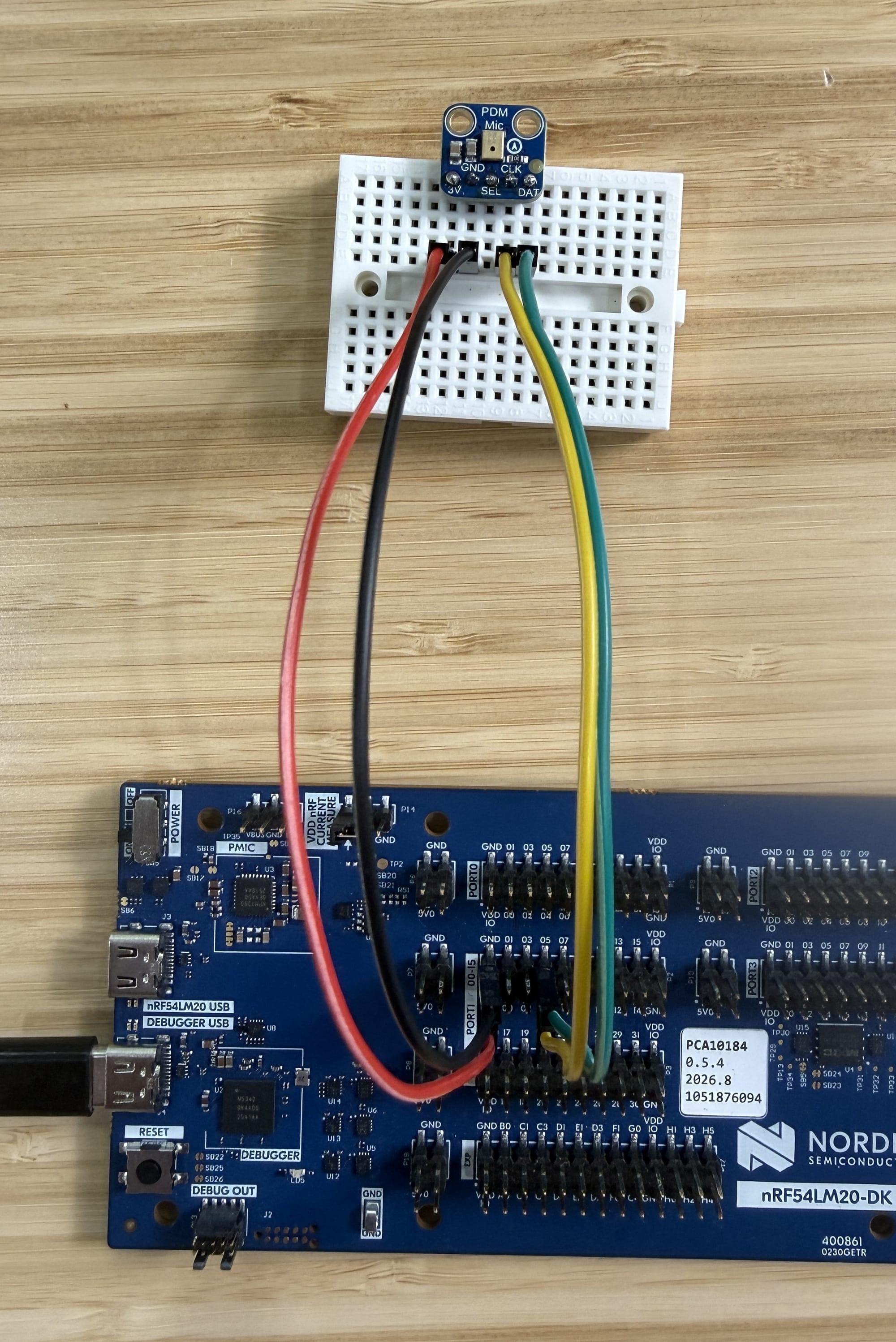 Adafruit 3492 PDM mic on a breadboard wired to the nRF54LM20 DK's expansion header with four jumpers: 3V (red), GND (black), CLK (yellow) to P1.04, DAT (green) to P1.05.