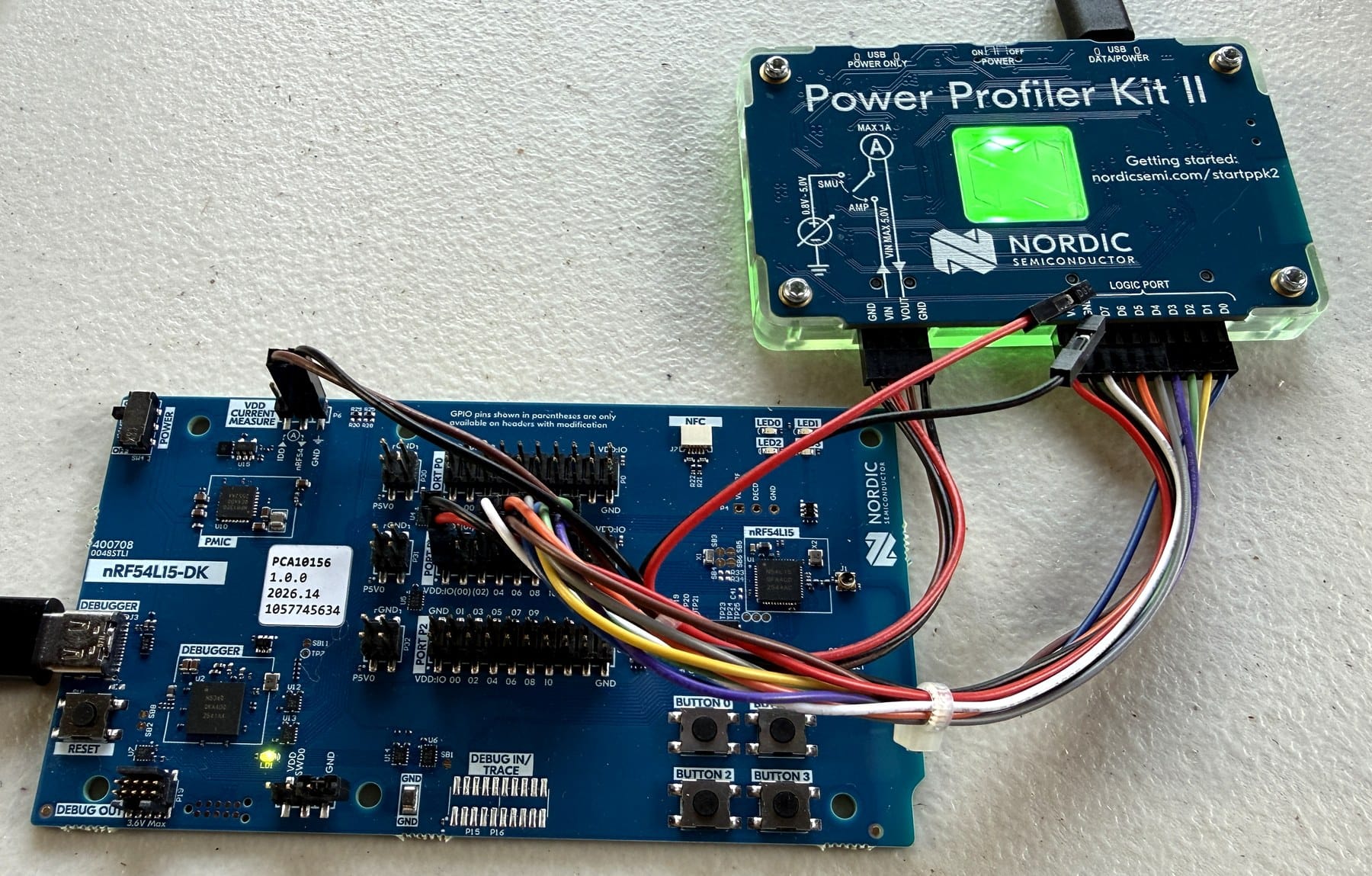 An nRF54L15-DK development kit wired to a Nordic Power Profiler Kit II on a workbench, with power leads into the kit's VIN, VOUT and GND terminals.
