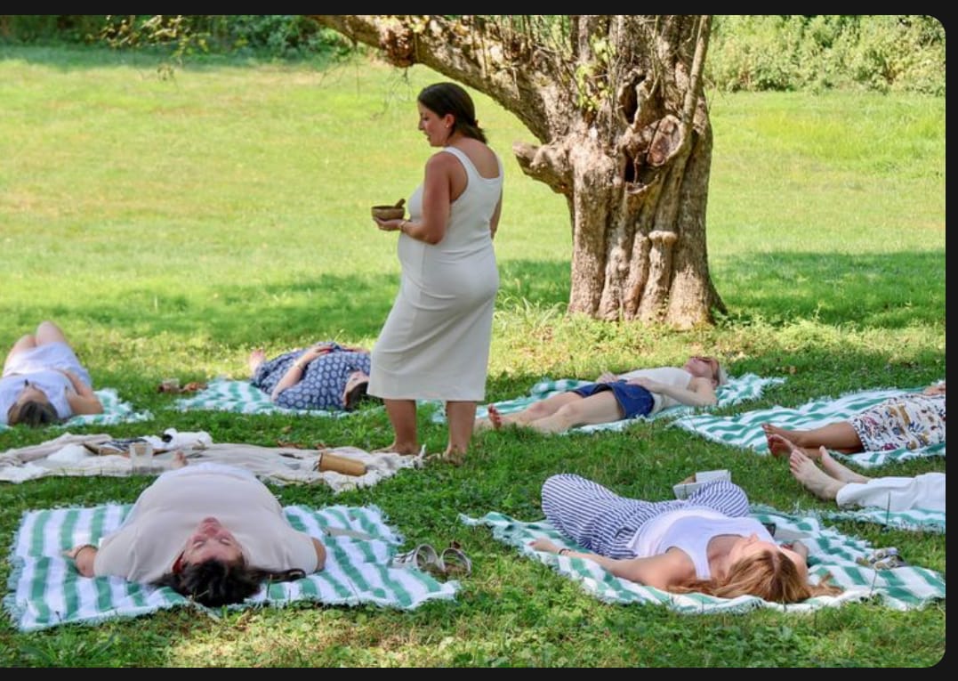 Women resting on green-striped towels under a tree in the grass