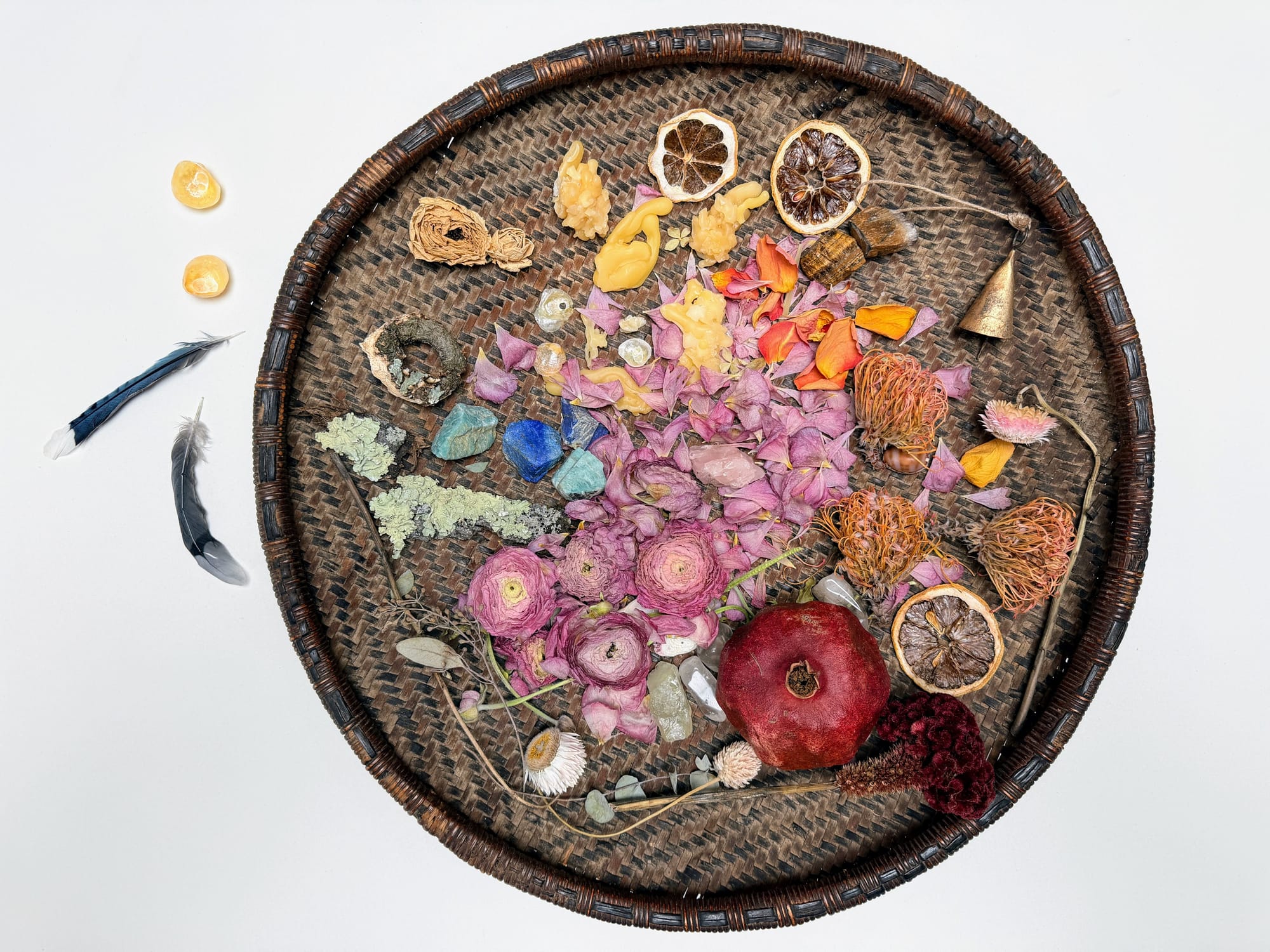 A collection of stones, dried fruit, flowers & feathers in a woven brown flat basket.