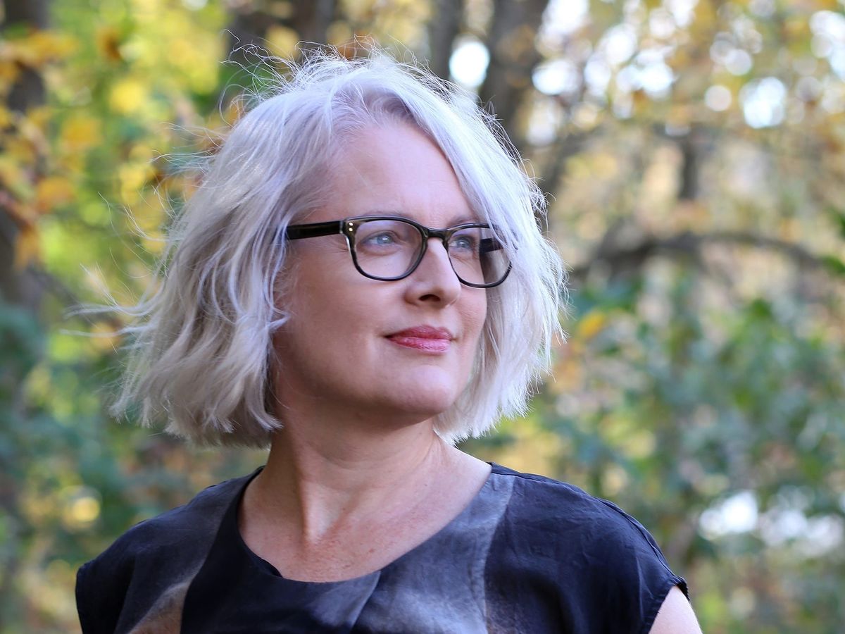 Grey-haired woman with glasses and a colorful shirt looks off into the distance