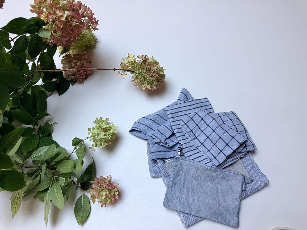 Indigo dyed tea towels and a cotton pouch lay near a bough of cut hydrangeas 