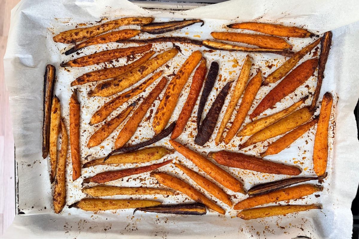 Roasted yellow, orange and purple roasted carrots in a single layer lay on top of parchment.