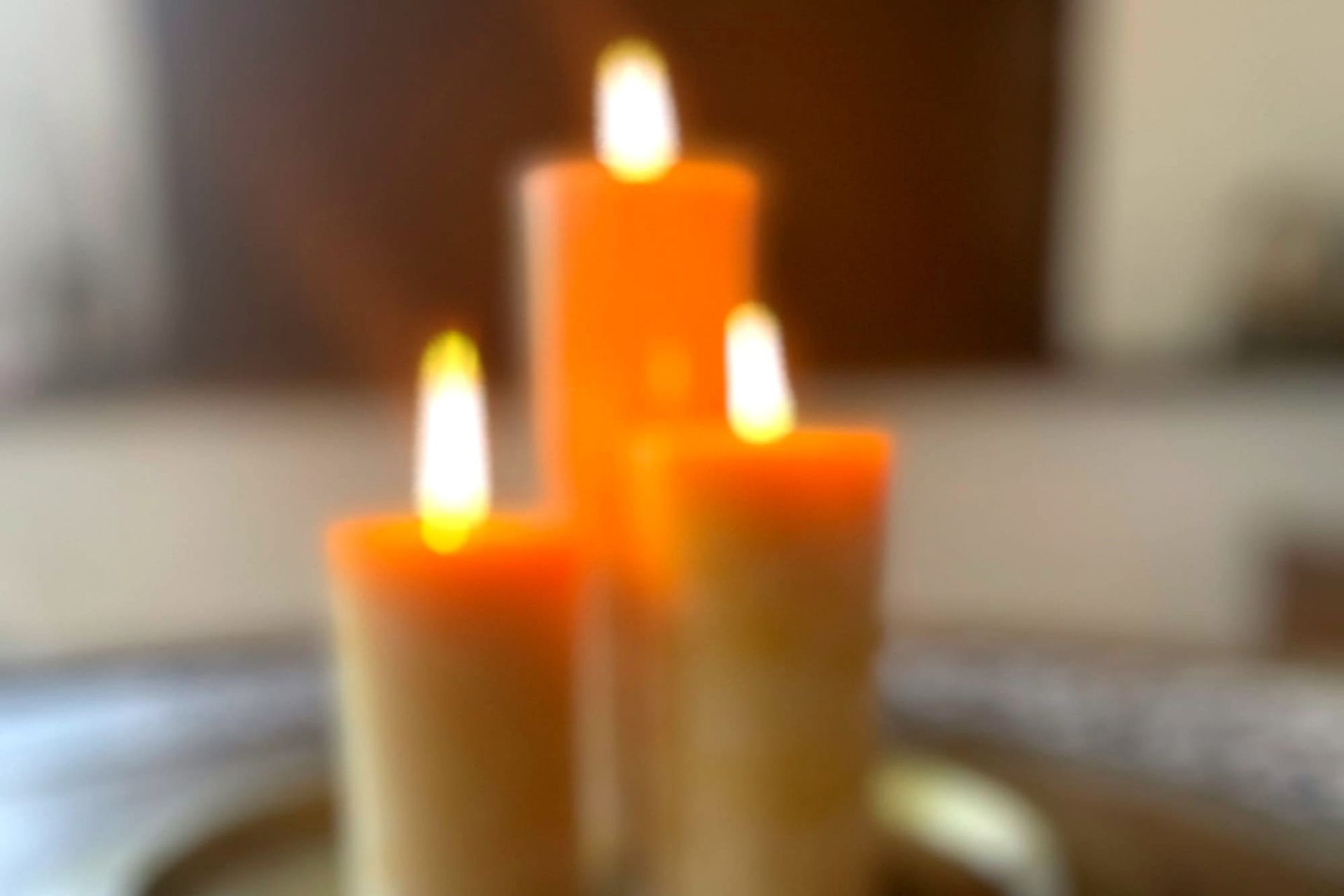 A blurred image of three beeswax pillar candles burn brightly.