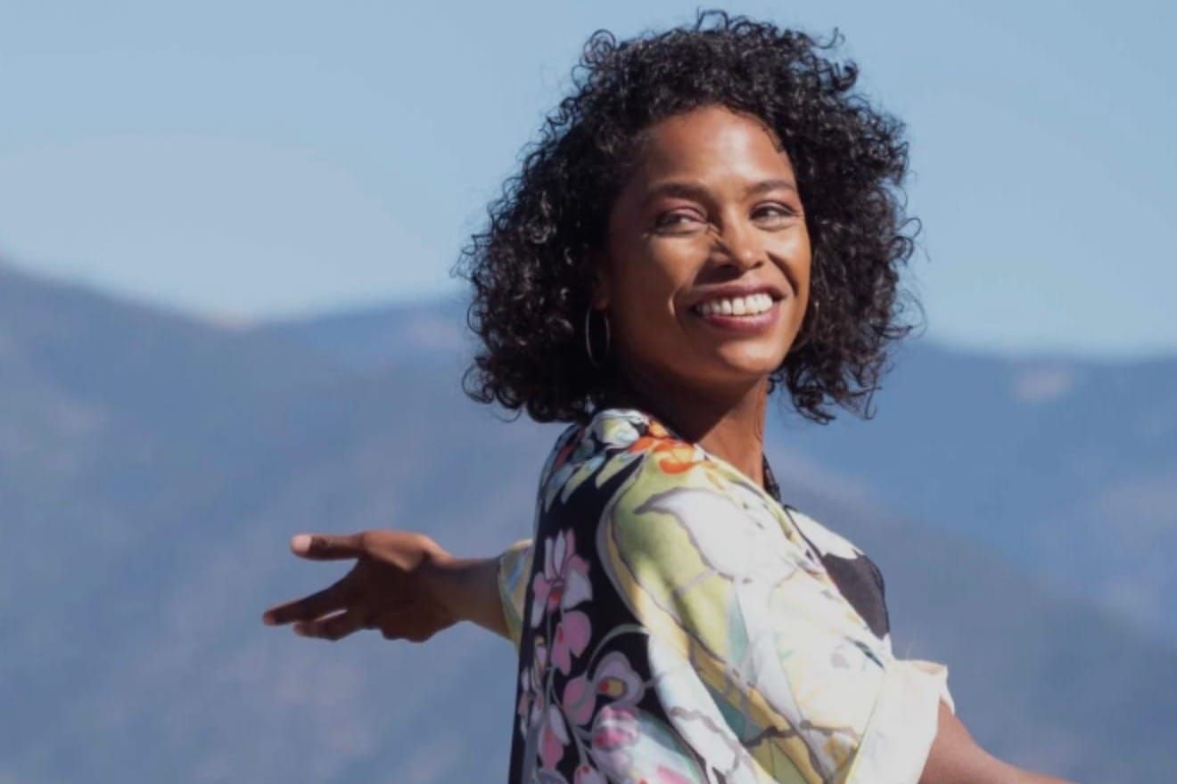 A black woman with with arms stretched outwards smiles with gorgeous energy