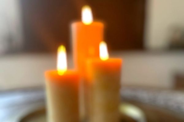 A blurred image of three beeswax pillar candles burn brightly.
