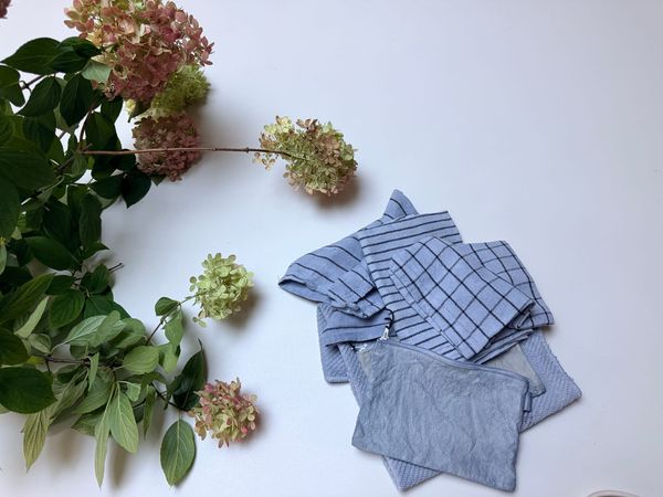 Indigo dyed tea towels and a cotton pouch lay near a bough of cut hydrangeas 
