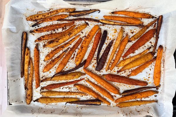 Roasted yellow, orange and purple roasted carrots in a single layer lay on top of parchment.