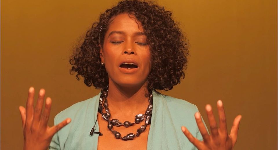 A black woman with hands open, palms facing her with eyes closed takes a deep breath