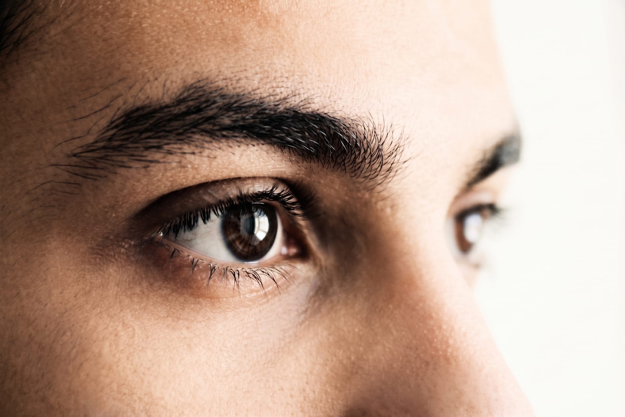 A photorealistic extreme close-up of a young man's eye and brow. His head is turned to the viewer's right, with his gaze fixed straight ahead.