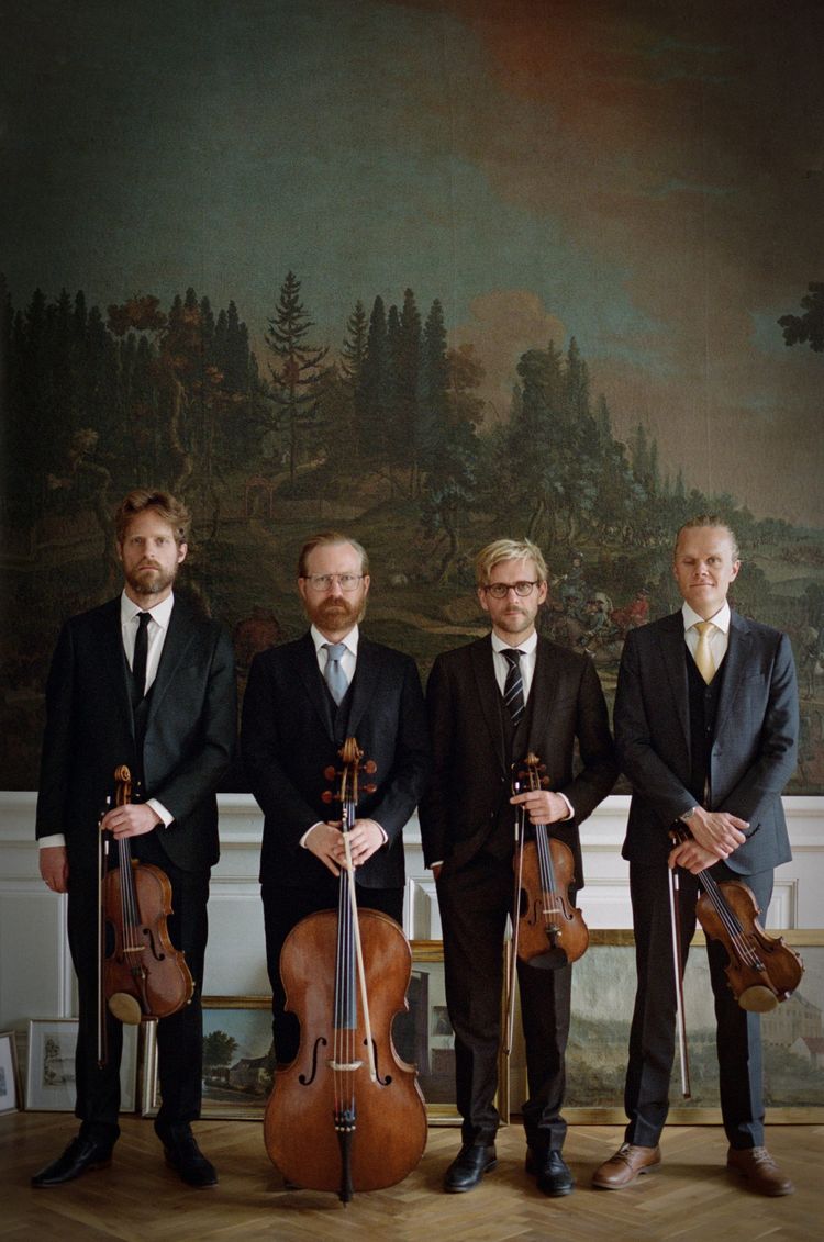 The Danish String Quartet. Press photo of a string quartet standing with their instruments in front of a dreamy forest landscape painting.