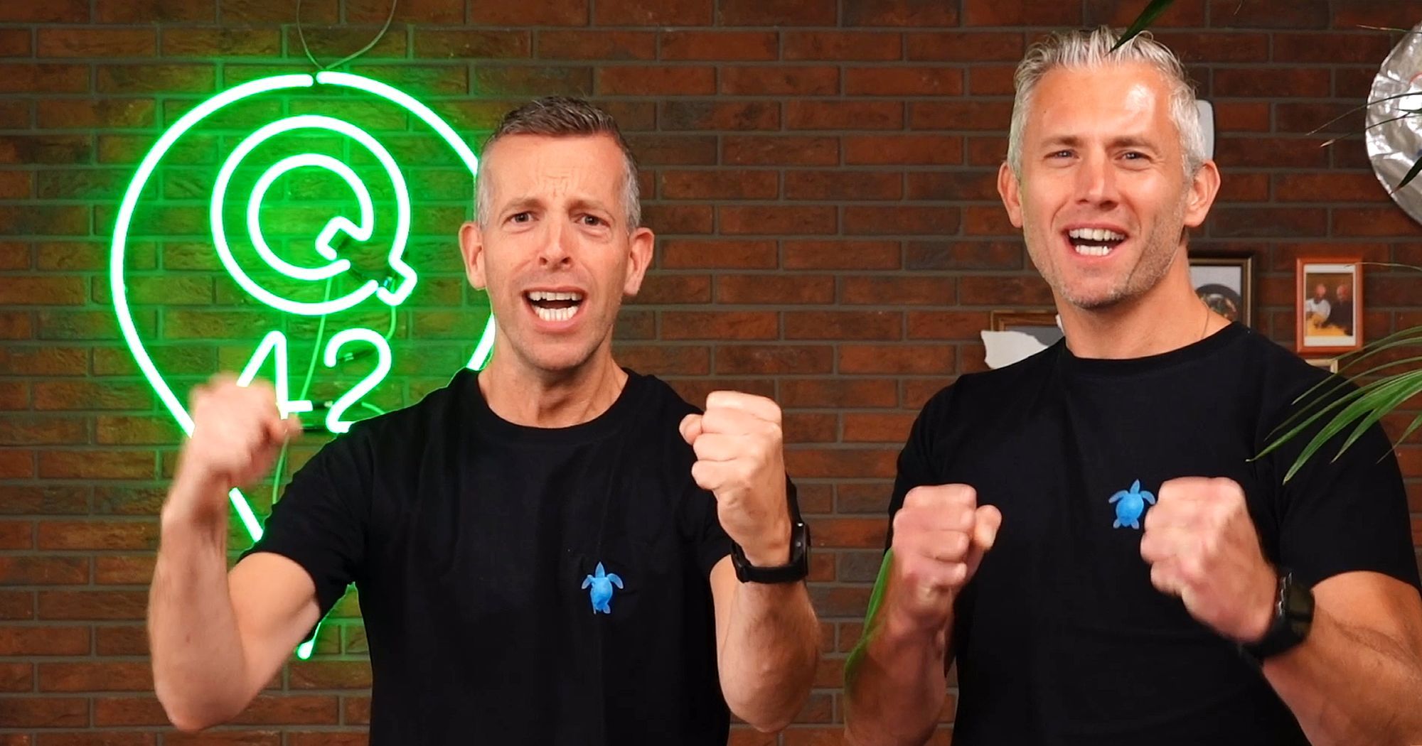 Twee juichende mannen met zwarte shirt tegen een bakstenen achtergrond met een groen Q42 logo.
