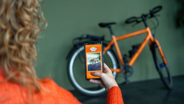 Vrouw met oranje trui en mobiele telefoon in de hand, waarmee ze een foto van een oranje fiets maakt.