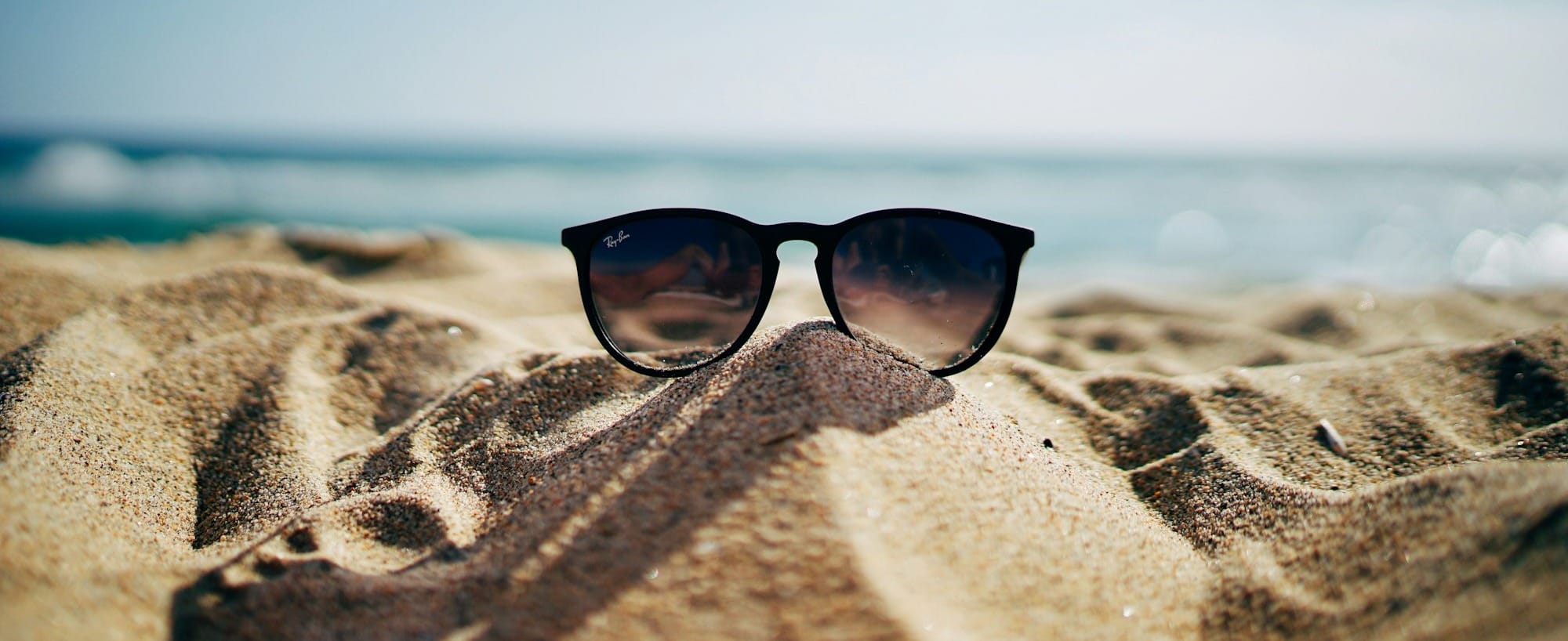 black Ray-Ban Wayfarer sunglasses on beach sand