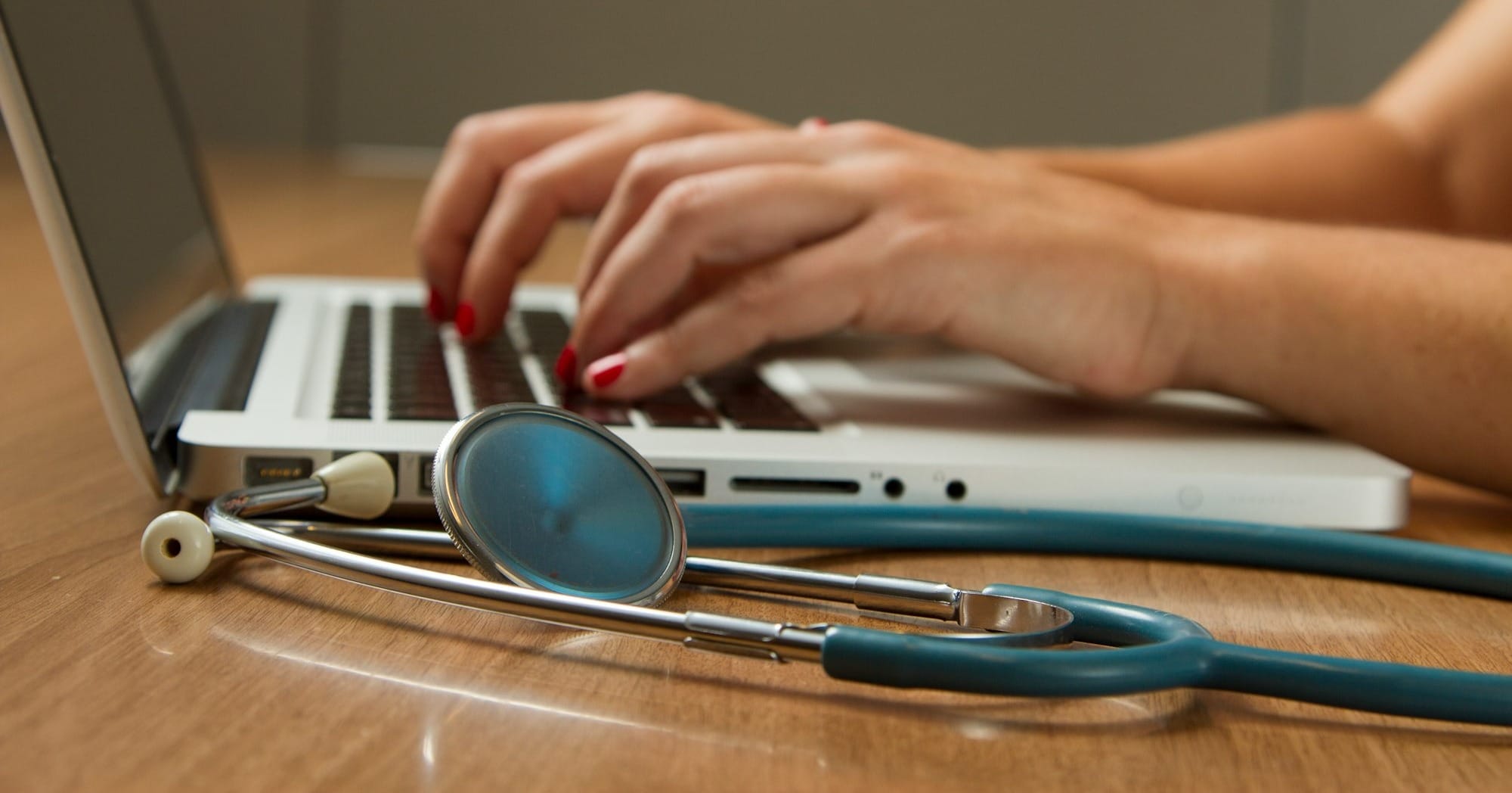 person sitting while using laptop computer and green stethoscope near