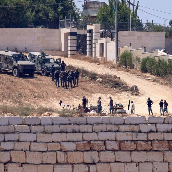 Israeli soldiers stand between settlers and Palestinian houses in the village of Qusra in the occupied West Bank on August 12, 2026.
