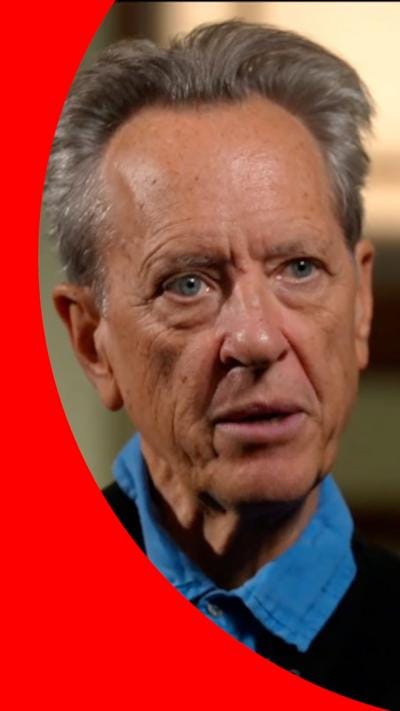 Actor Richard E Grant wearing a dark coat and light blue collared shirt