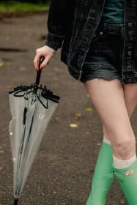 Woman in rain boots holding a clear umbrella