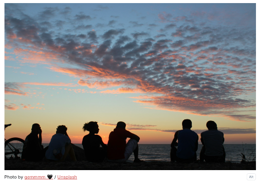 Silhouettes of youp people looking at the sunset on the horizon.