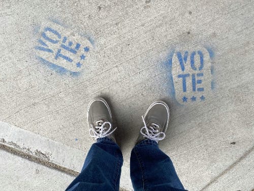 Shoes on the sidewalk near stencils that say VOTE.