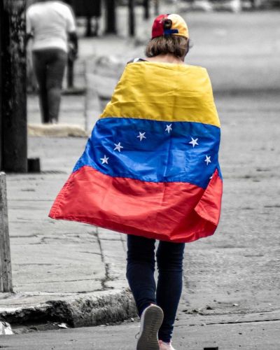 A woman walking down the street wrapped in a Venezuelan flag.