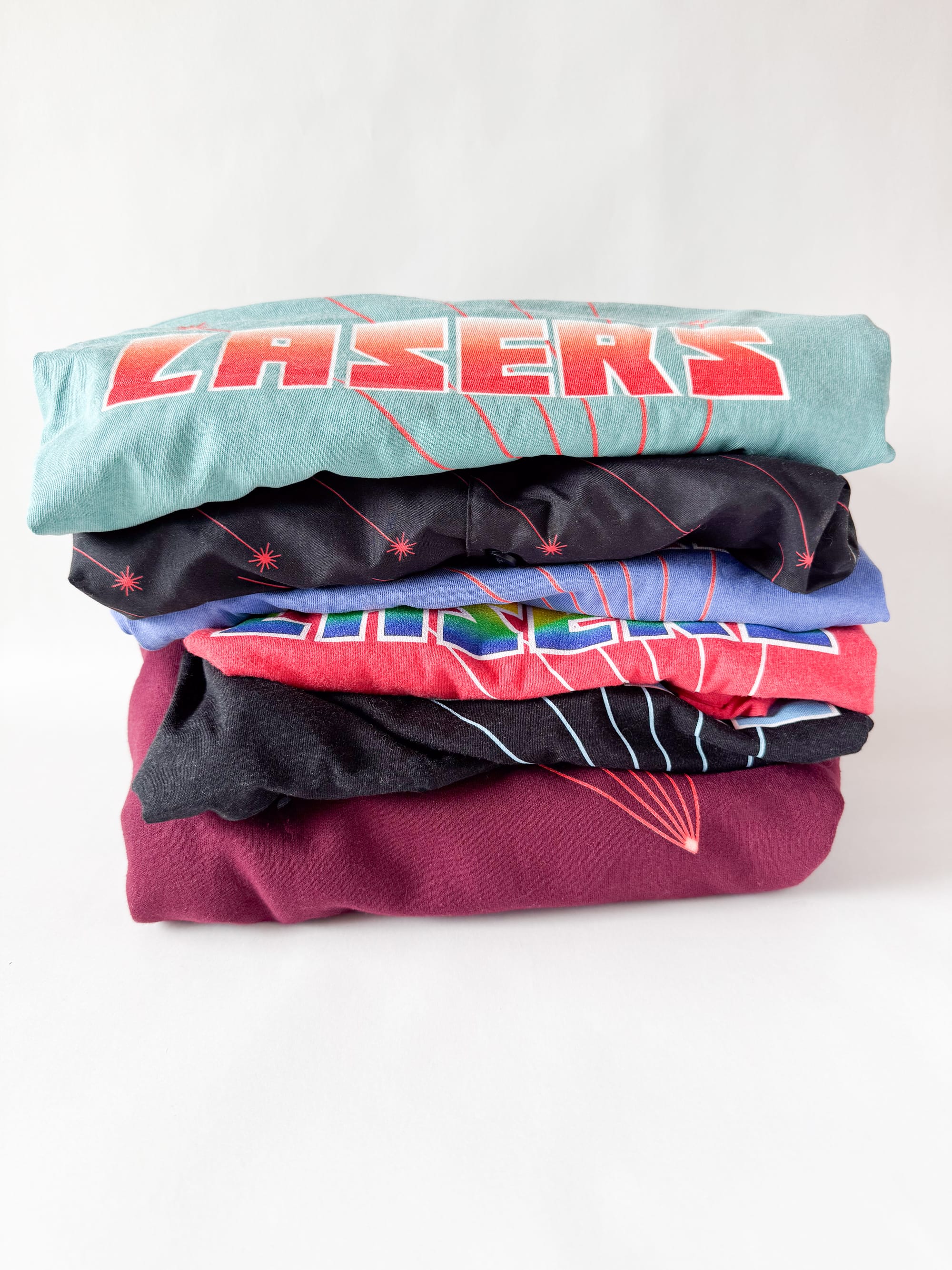 Stack of two tank tops, two t-shirts, a button-down shirt, and a hoodie, all with laser designs on them. There are no cats or cat hairs in sight.