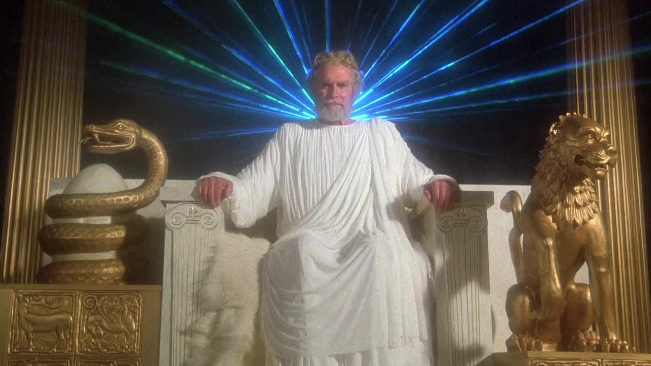 Zeus (Lawrence Olivier) sits on his throne with rays of brilliant green and blue fanning out behind his head.
