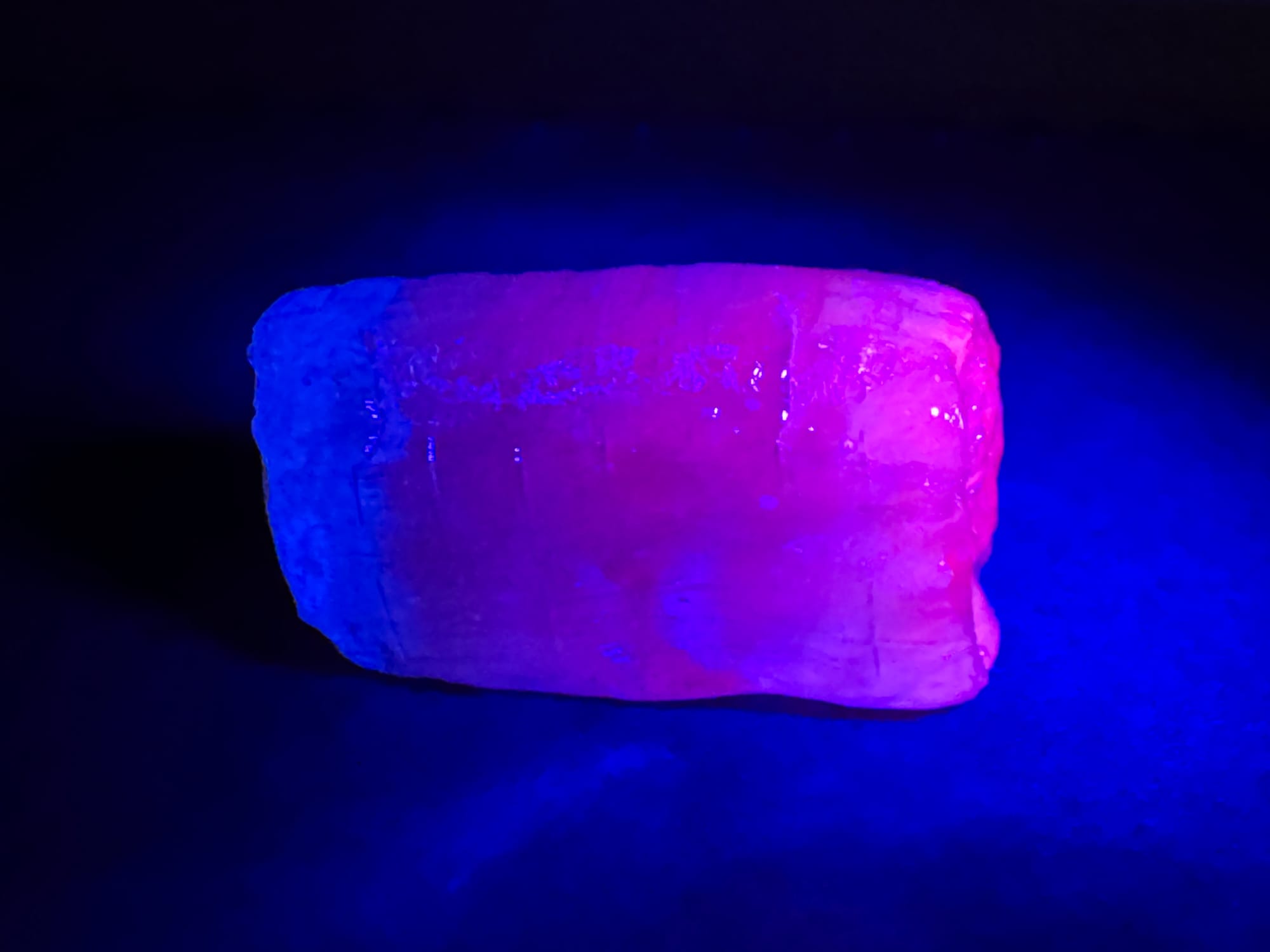 An unwrapped piece of jolly rancher candy with a UV flashlight illuminating it from one end. The illuminated end is hot pink, while the shadowed areas are deep blue.