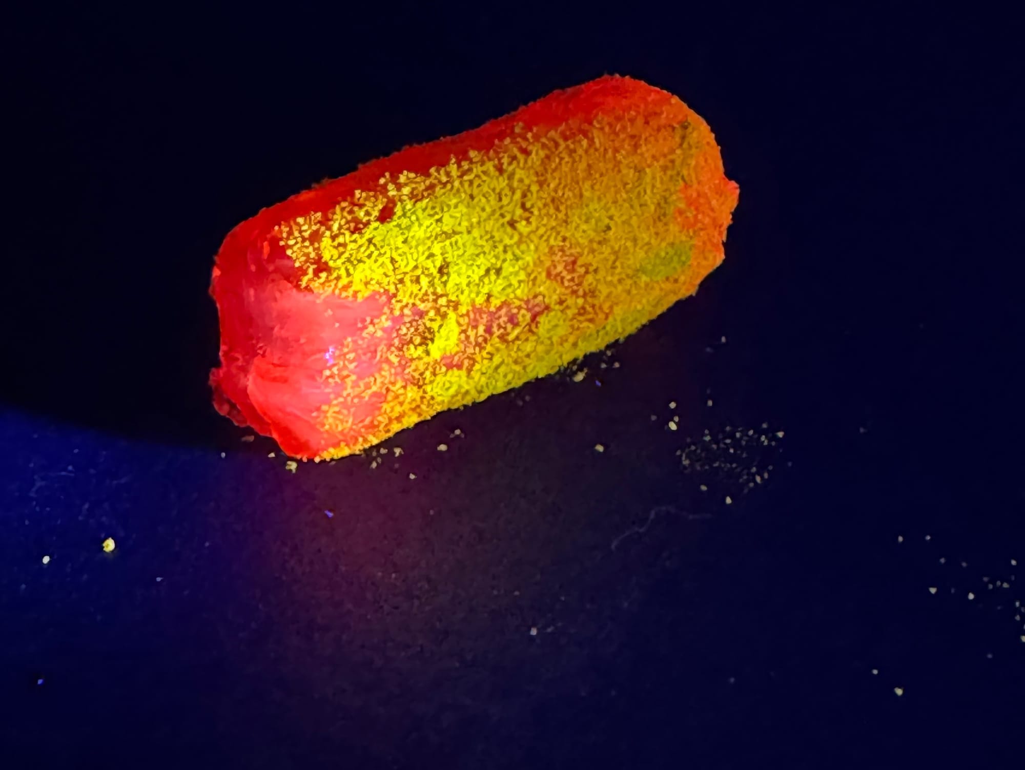 The candy is glowing red and the turmeric coating is glowing yellow. It's hard to say which is glowing more brightly.