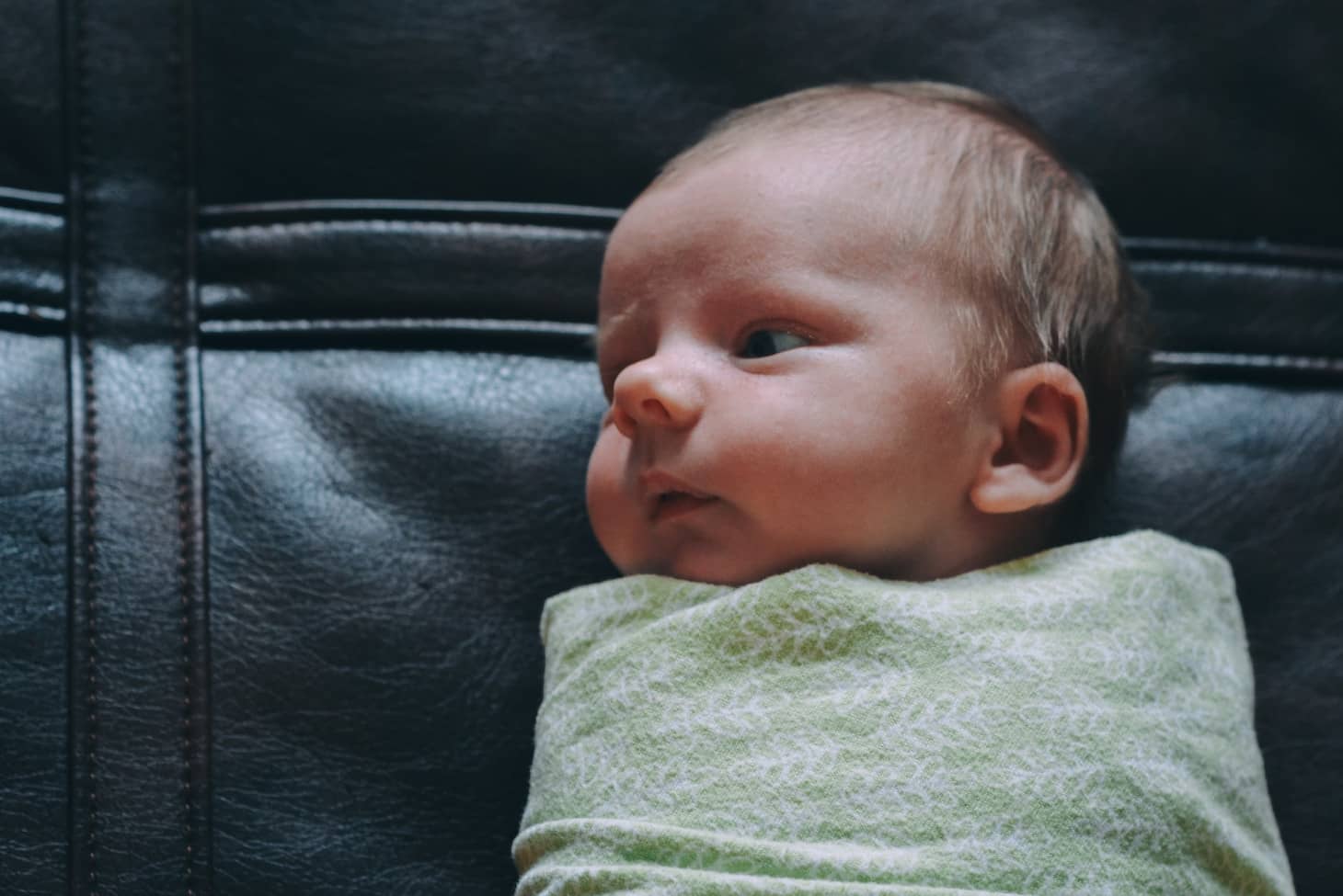 recién nacido envuelto y sentado sobre un sofá de cuero