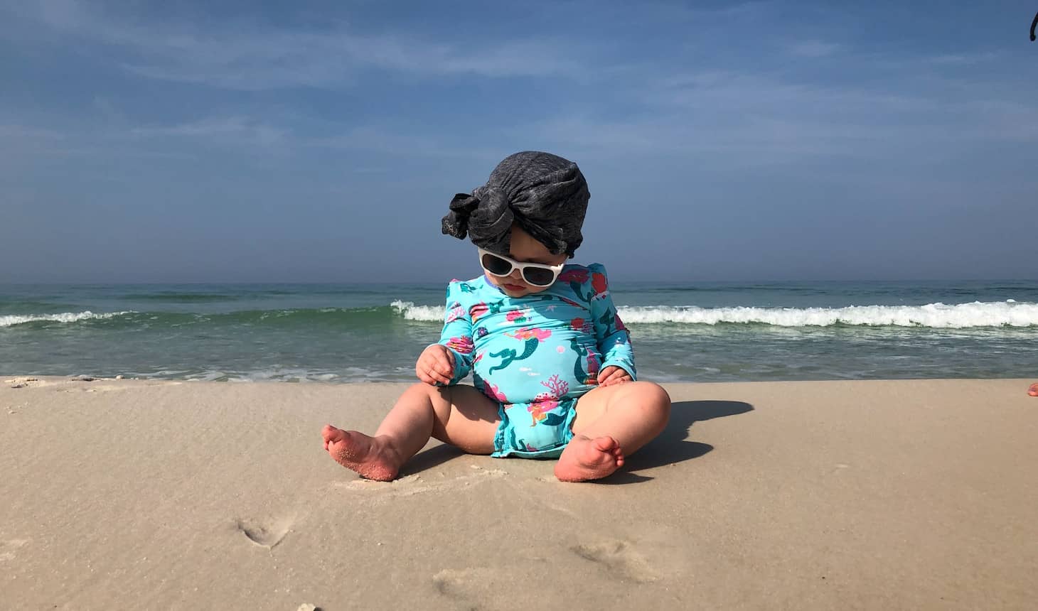 bebé con gafas de sol en la orilla del mar