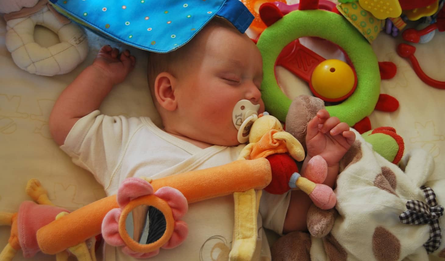 bebé dormido con un chupete y debajo de sus juguetes