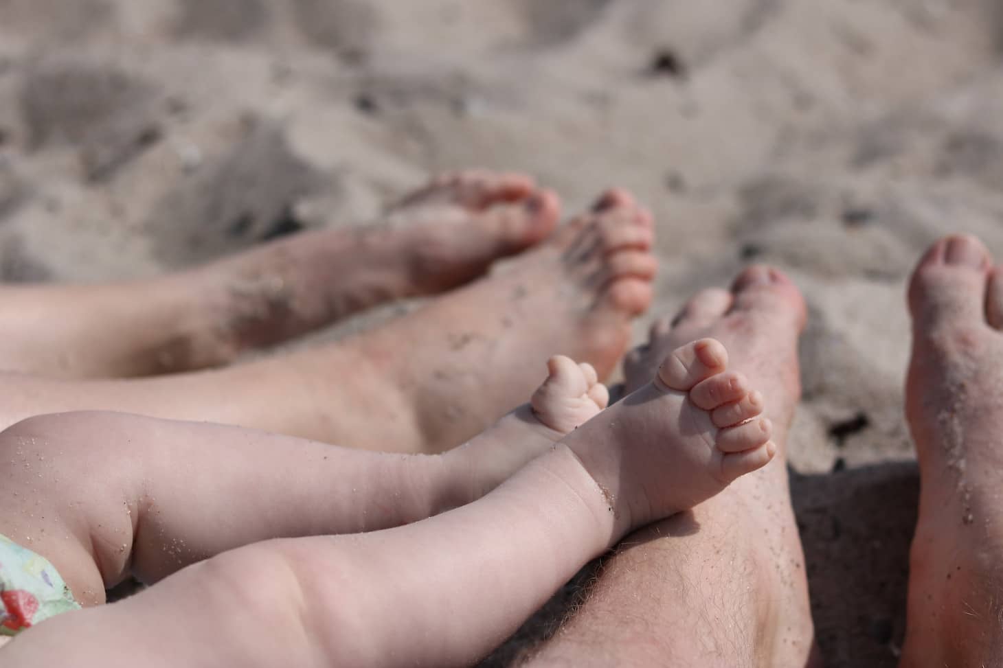 las piernas de un bebé encima de su papá en la playa