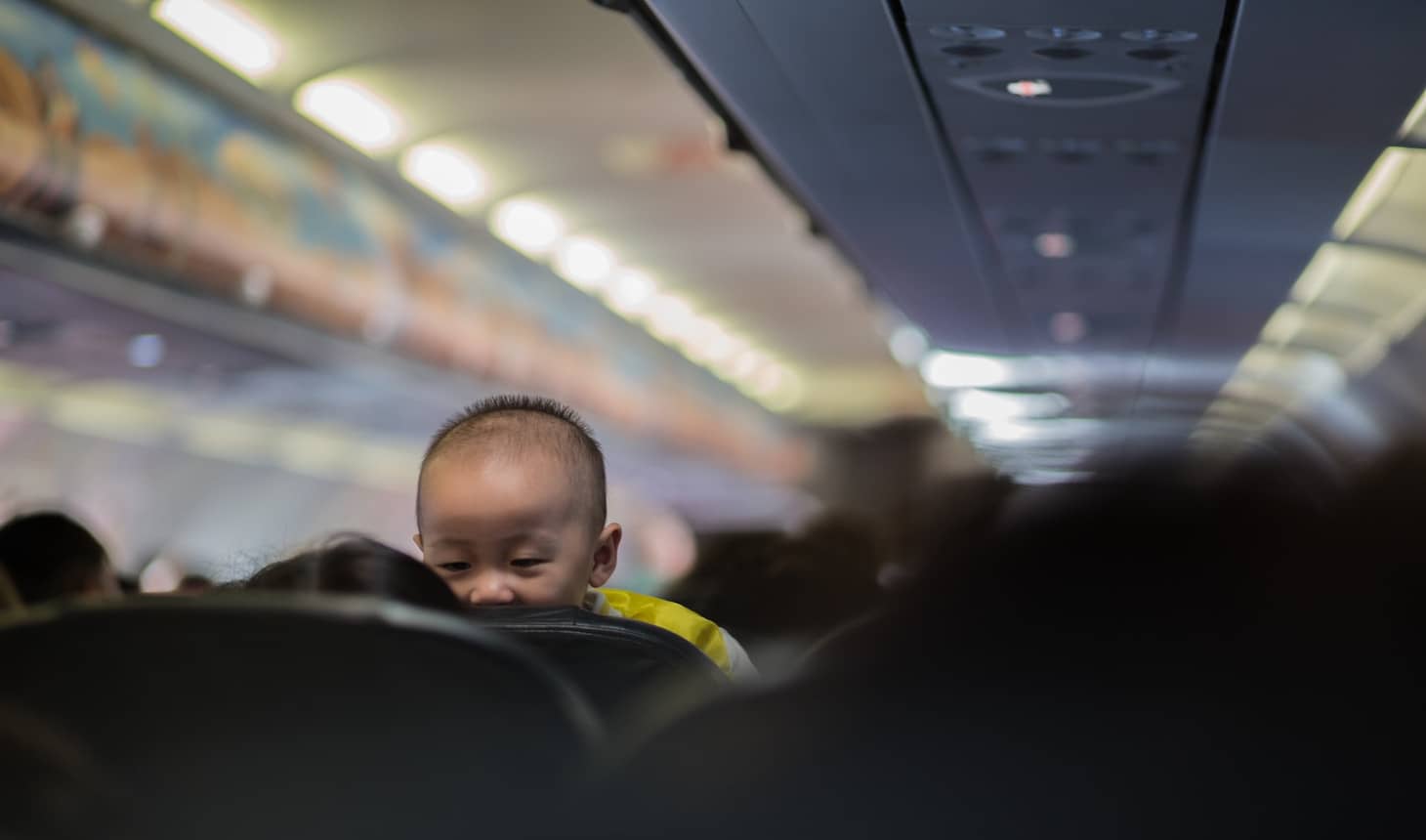 la cabecita de un bebé asomando por encima de los asientos de un avión
