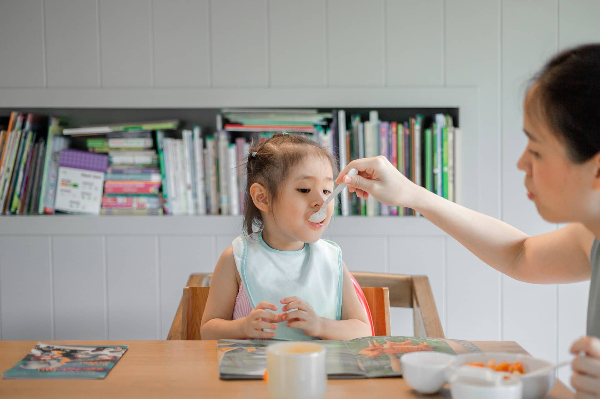 niña pequeña en la mesa y su madre le da de comer