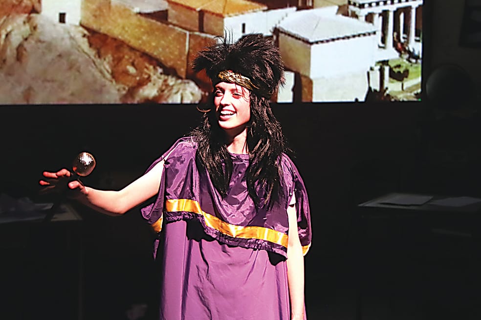 Poppy Cann as Sophocles in a talk show host scene.