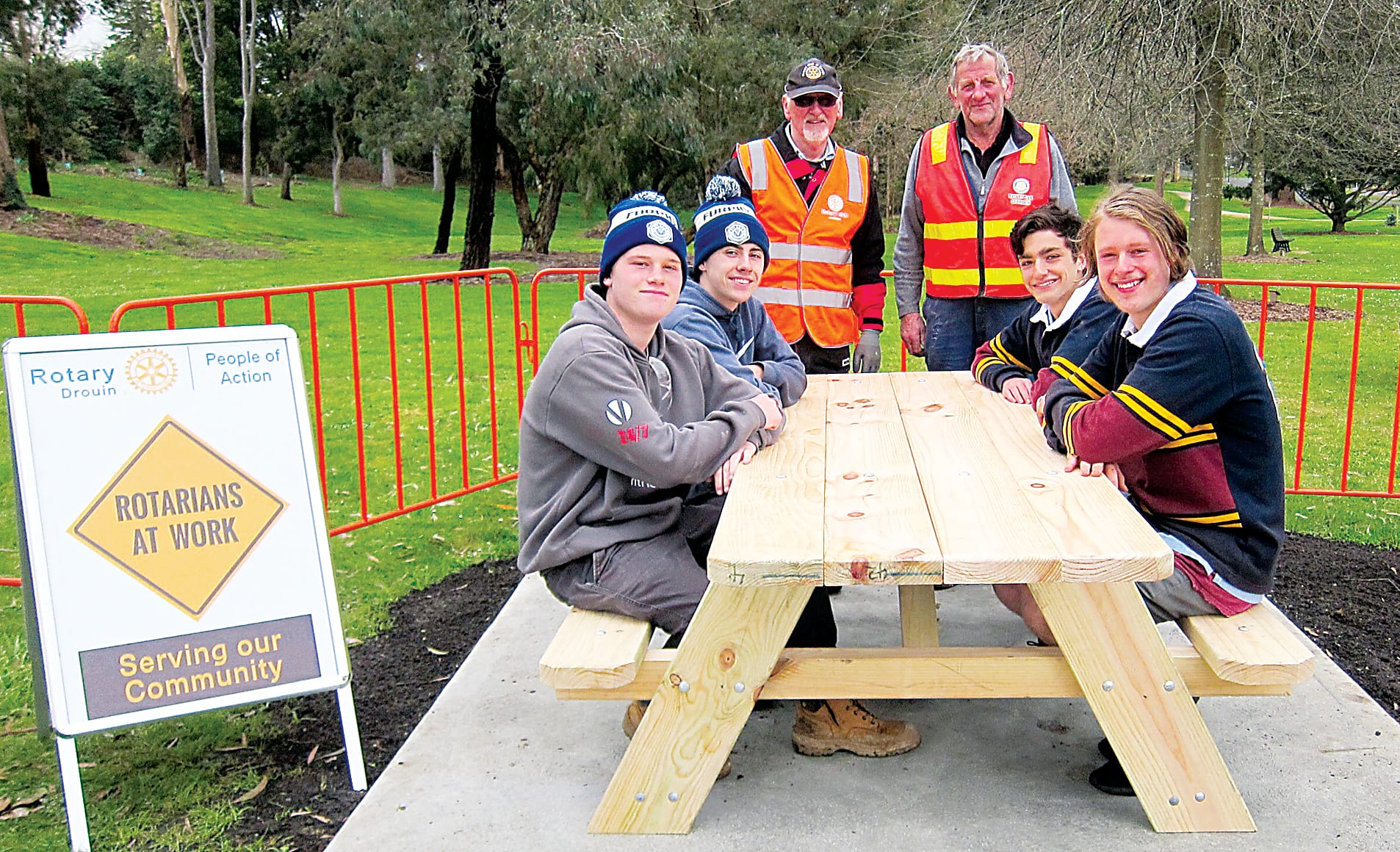 A job well done. Drouin Secondary College VCAL students, from left, Zane Atkinson Gill, Keith Stirling, Nach Whyman and Oscar Ennis-Wert (absent Mo Jafari) try out the new picnic table and seating they built and installed at Drouin's Alex Goudie Park with the support of Rotarians Roger Playdon (standing at left) and Bill Petschack.