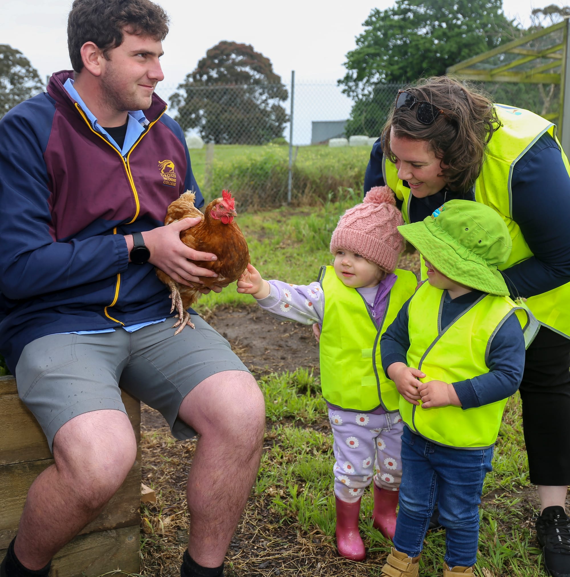 Drouin Secondary College student Riley D'laney and Little Saints educator Caitlyn Ginnivan help Page Barr pat the chicken while Axel Wright watches on.