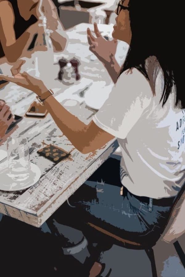 Stylized image of a woman with black shoulder-length hair, a white tshirt, blue jeans sitting with friends at a table talking animatiedly.