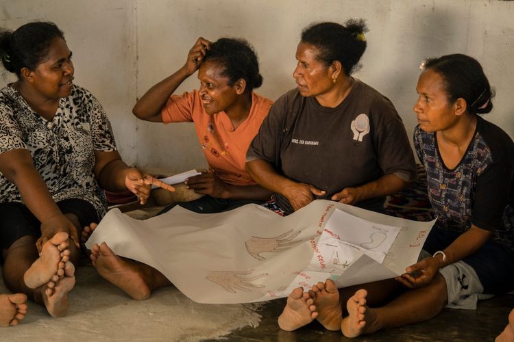 A group of four Indigenous Papua women seated on the floor, discussing a large picture for a workshop